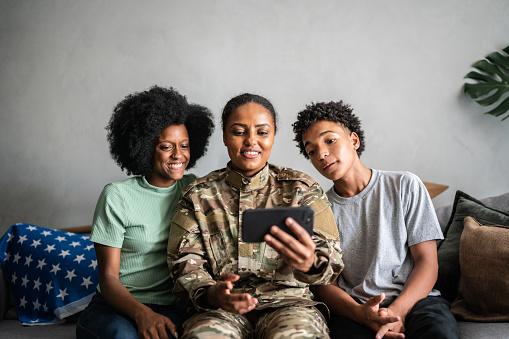 Soldier mother with daughter and son on a video call (or taking a selfie) on the mobile phone at home