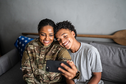 Soldier mother with son on a video call (or taking a selfie) on the mobile phone at home