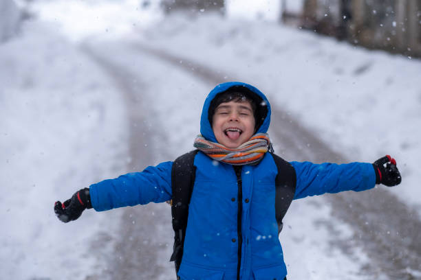 istock Funny little boy in blue winter clothes walks during a snowfall. 1387533436