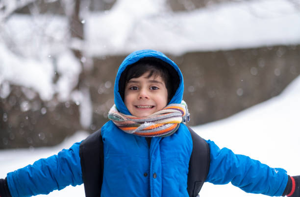 istock Funny little boy in blue winter clothes walks during a snowfall. 1387533537