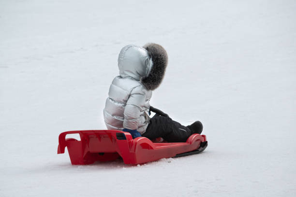 A young kid skates with a plastic red sled on a winter slide