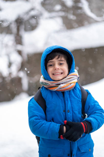 istock Funny little boy in blue winter clothes walks during a snowfall. 1387534084