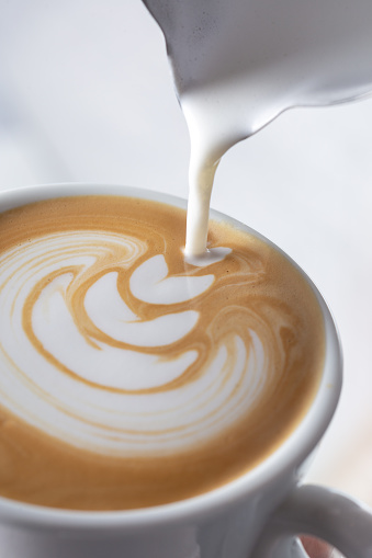 Barista pouring latte foame over coffee, espresso and creating a perfect cappuccino