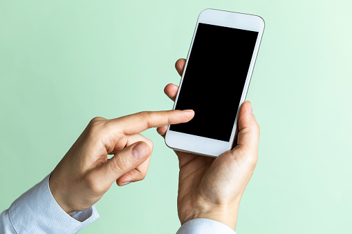 Unrecognizable person is showing screen of smart phone to camera and is pointing with one finger at device screen in front of green background.