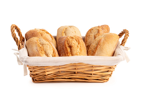 Freshly baked wheat buns in a wicker basket isolated on a white background. Fresh tasty bread in a wattled traditional basket with white napkin and handles.