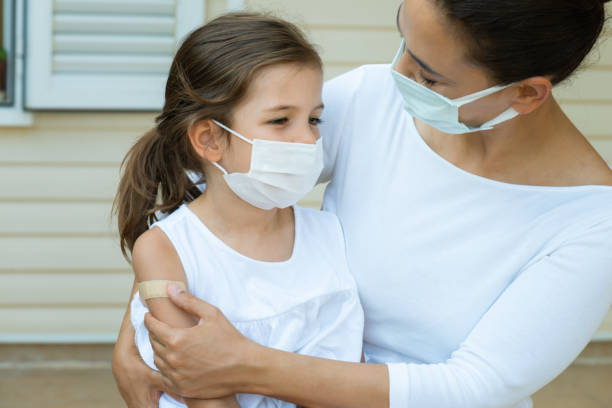 Vaccination Child with protective face mask is sitting in her mothers lap. They are looking at eachother. hepatitis photos stock pictures, royalty-free photos & images