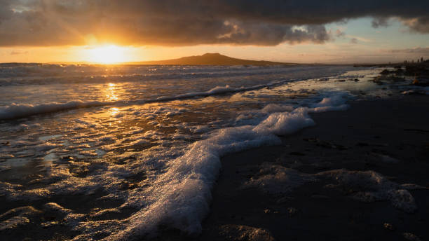 Sunrise over Rangitoto Island, sea foams catching sunlight at foreground, Takapuna Beach, Auckland. Sunrise over Rangitoto Island, sea foams catching sunlight at foreground, Takapuna Beach, Auckland. rangitoto island stock pictures, royalty-free photos & images