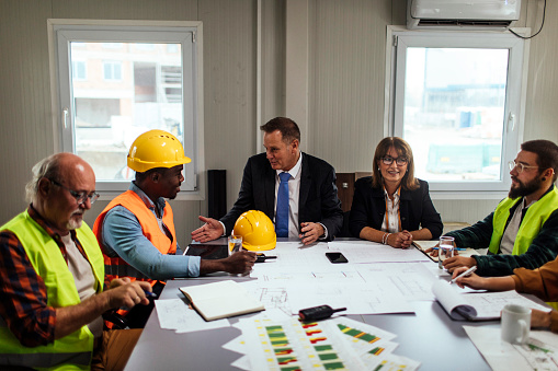 Investors and construction workers discussing architectural plans in the office together