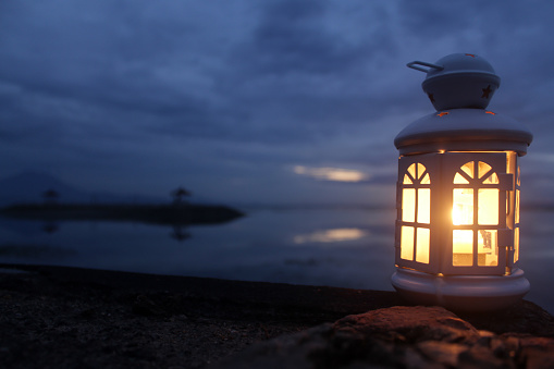 Light of lantern on a rock with blue background of the night sky and clouds over the sea horizon at dusk blue hour. Copy space for your inspirational text design.