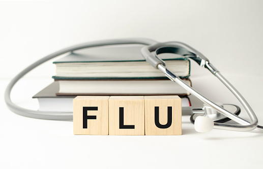 the word flu is written on wooden cubes near a stethoscope on a paper background. medical conceptual word collected of wooden elements with the letters.