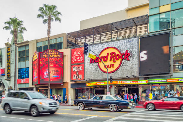 Cars and pedestrians move past Hard Rock Cafe and TCL Chinese Theatre on Hollywood Boulevard in Hollywood, Los Angeles, California, USA on a cloudy day.