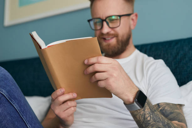 istock Cheerful man reading book at home 1387557474