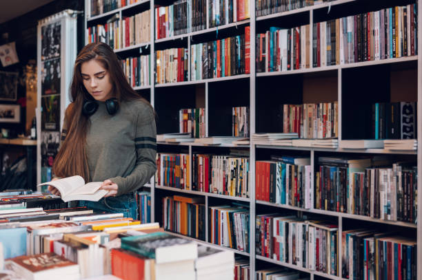 Woman buying books at a bookstore Young female customer reading a book in bookstore while buying some good literature. Woman picking a book to read. book store stock pictures, royalty-free photos & images