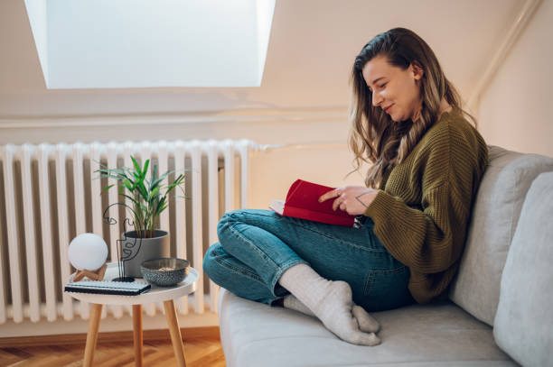 istock Woman reading a book while sitting on the couch at home 1387558379