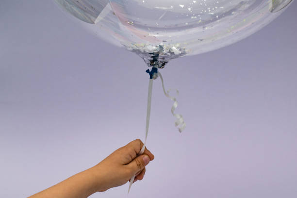 Child hand holding balloon Kid is holding helium filled transparent balloon with glitters. Copy space. helium balloon stock pictures, royalty-free photos & images