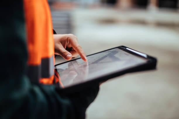 Nicht erkennbare Hände von Bauarbeitern, die ein digitales Tablet halten, während sie im Freien arbeiten