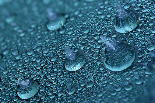 photo of irregularly shaped water droplets with various shapes on a black surface. lots of water drops on a plastic background