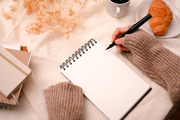 istock Female blogger in cozy sweater writing something on empty spiral notepad 1387570320