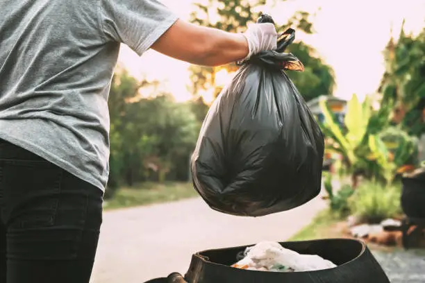 Photo of hand holding garbage black bag putting in to trash