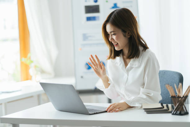 istock Excited asian lady having video call at work place, using laptop and graph on wihteboard behind, copy space. Happy woman waving at laptop screen, attending video conference. 1387572711