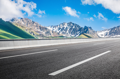 Asphalt road and snow mountain with beautiful sky clouds under blue sky. Road and mountain background.
