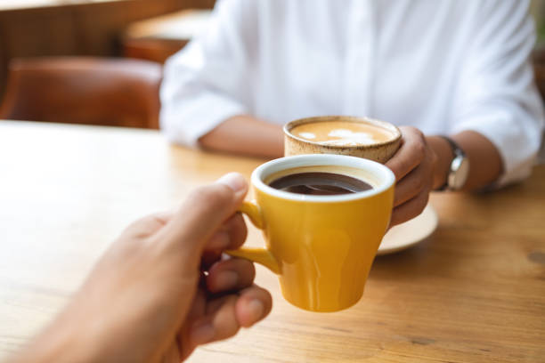 Closeup image of a young couple people clinking coffee cups together in cafe stock photo