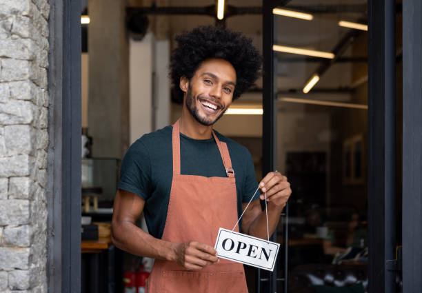 istock Happy waiter holding an open sign at a cafe 1387578813