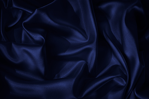 Navy blue silk satin. Beautiful wavy folds. Dark elegant background with space for design. The surface of the fabric.