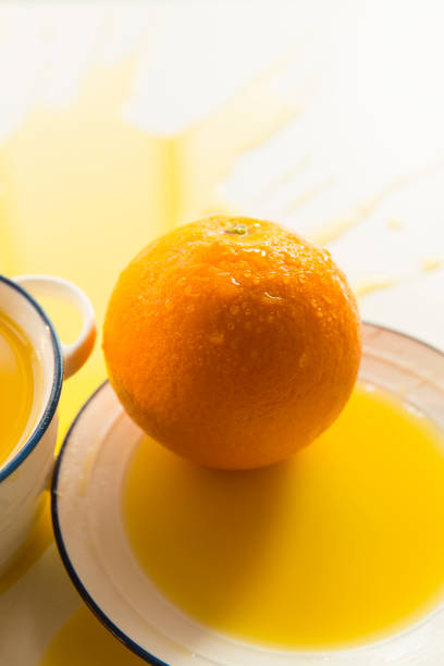 Whole orange with dew ,spilled orange juice, porcelain tureen and plate on white background.