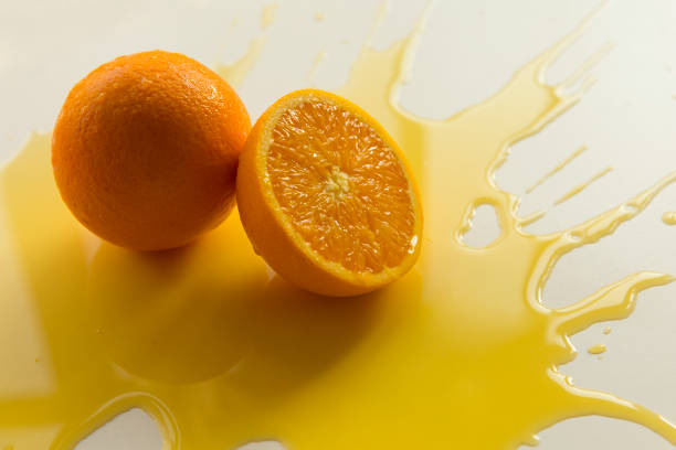 Halved and whole oranges with spilled orange juice on white background.