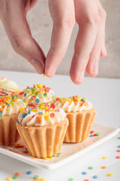 istock Hand is sprinkling mini cupcakes decorated with candy. 1387594988