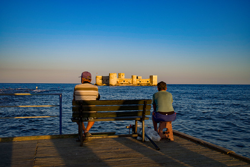 18 October 2021 Turkey Mersin city Old man and young man watching the Maiden's Castle at sunset