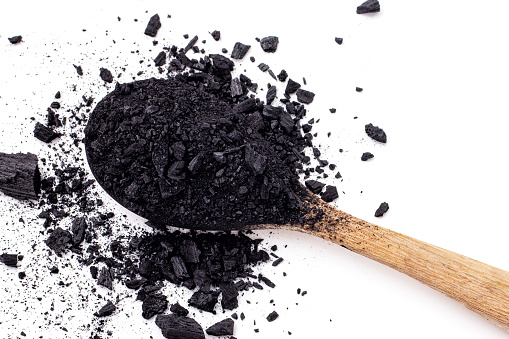 Small pieces of charcoal and charcoal powder was placed on a wooden spoon and scattered on a white background.