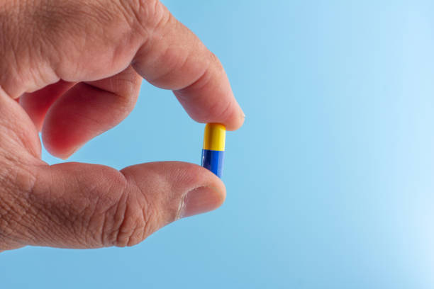 istock Hand is holding an antibiotic capsule (blue-yellow) isolated on a blue background. 1387611585