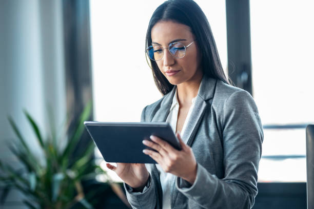 istock Beauty business woman using her digital tablet while sitting on a desk in a modern startup office. 1387612817