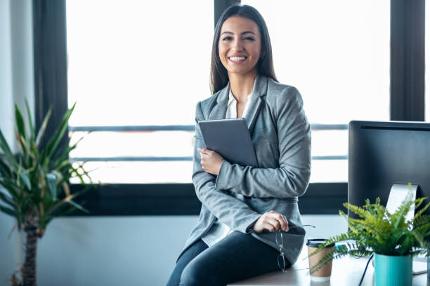 istock Beauty business woman using her digital tablet while sitting on a desk in a modern startup office. 1387612839