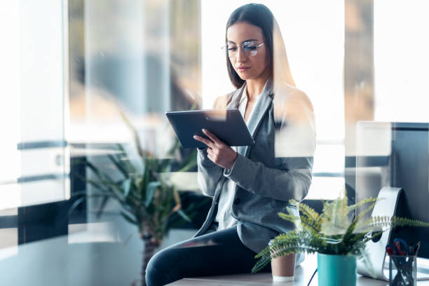 istock Beauty business woman using her digital tablet while sitting on a desk in a modern startup office. 1387613050