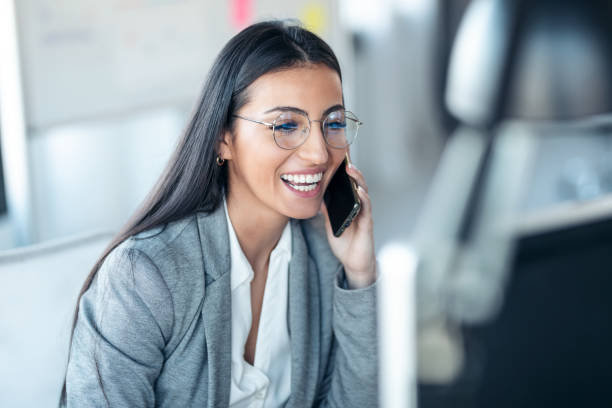 사무실에서 노트북으로 작업하는 동안 휴대 전화로 이야기하는 아름다운 비즈니스 여성. - back office 뉴스 사진 이미지