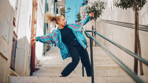 professionelle junge erwachsene frau in lässiger stilvoller kleidung breakdance hip hop auf der straße einer altstadt in einer stadt. szene, die in einer städtischen umgebung auf einer ruhigen kleinstadttreppe gedreht wurde. - city life funky cool urban scene stock-fotos und bilder