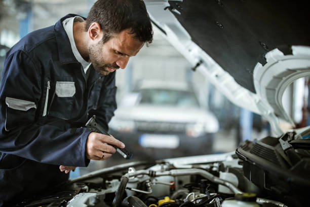 istock Auto mechanic examining car with a lamp in a workshop. 1387619353