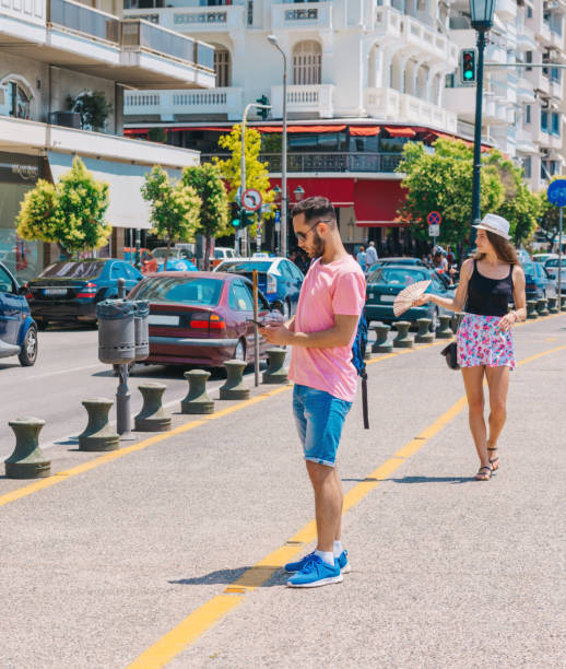 istock Student calling a taxi while wearing a backpack on his shoulder and standing on a city boardwalk. 1387620408