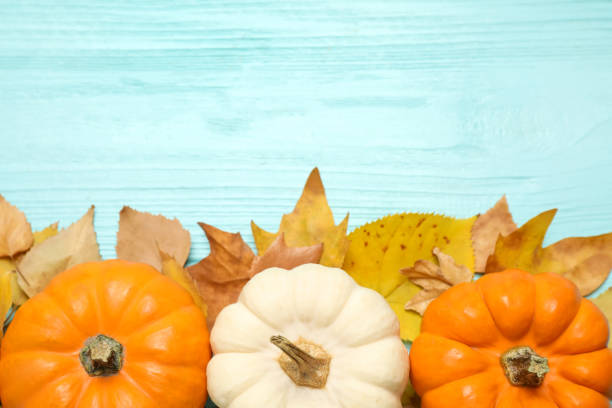 istock Flat lay composition with pumpkins and autumn leaves on light blue wooden table. Space for text 1387621855