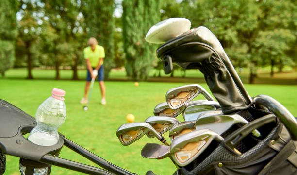 golfista su un campo da golf, pronto a giocare. golfista con mazza da golf che colpisce la palla per il colpo perfetto. in primo piano, il golf cart con la borsa e le mazze da golf - golf swing golf golf club golf ball foto e immagini stock