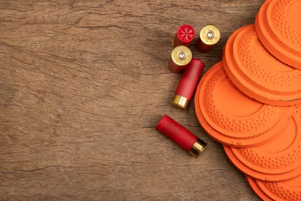 Photo of Flying clay pigeon target with shot gun bullet shell on wooden background , Gun shooting game