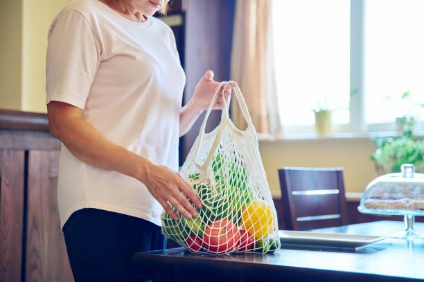 istock Fresh vegetables in mesh eco bag on table in kitchen, woman puts vegetables on plate 1387628811