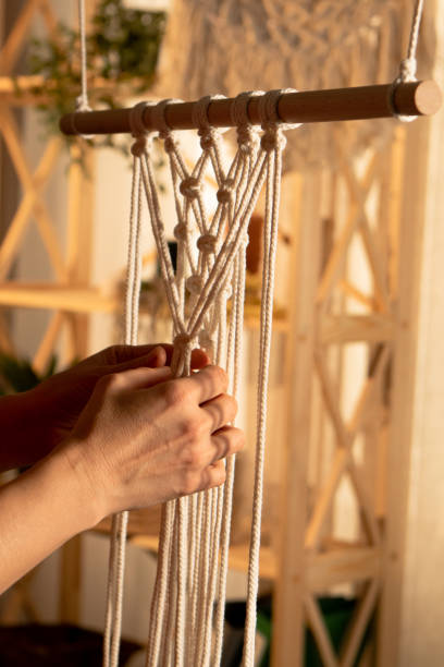 istock Women's hands weave a macrame pattern in Boho style. A woman ties knots on cotton threads to create lace. Creative workshop. Modern knitting natural decoration concept. Craft of rope. Close up 1387629464