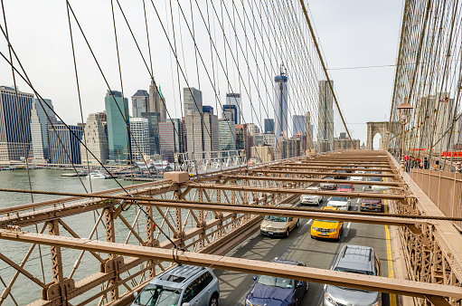 Different colored cars and taxi cab driving on Brooklyn Bridge New York City, wide angle shot, People walking in the middle of the bridge, One World Trade Center with construction area and crane on top in the background, horizontal