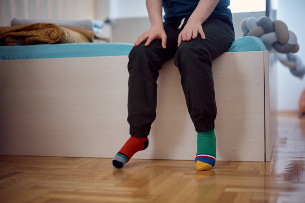 istock Unrecognizable down syndrome man with different color socks at home. 1387633676