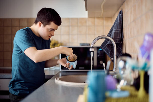 istock Man with down syndrome washing dishes in the kitchen. 1387633747