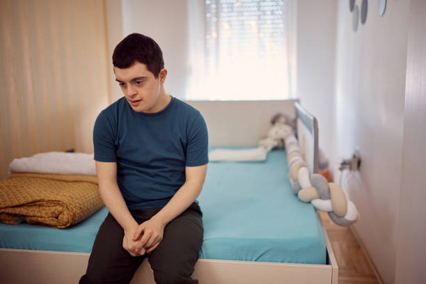 istock Young pensive man with down syndrome siting on his bed at home. 1387633880